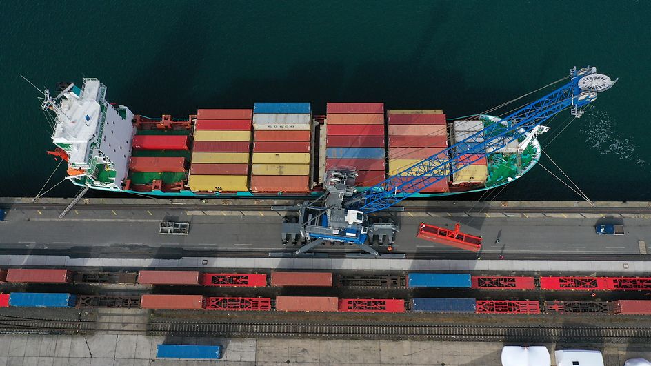 Symbolbild Lieferkettensorgfaltspflichtengesetz (LkSG): Container werden von einem Schiff auf Güterwagen geladen.