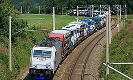 Eine Ellok der Baureihe 185 des EVU Lokomotion GmbH durchfährt mit einem Zug voller fabrikneuer Mercedes-Lkw zwischen Traunstei